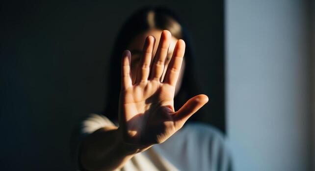 Woman shielding face with hand in gesture of protection, concept of defense and avoidance photo