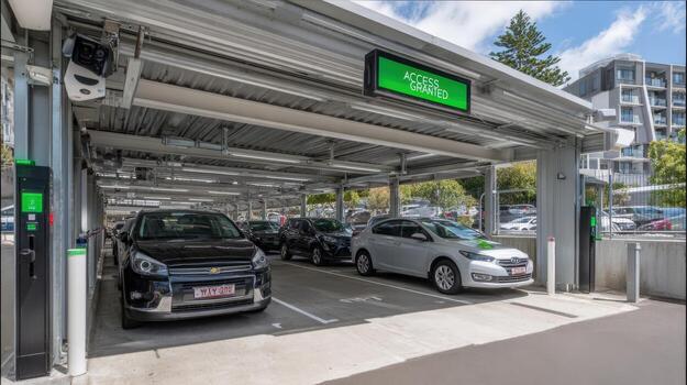 Modern parking garage featuring cars under a metal structure with an illuminated access sign on a sunny day photo