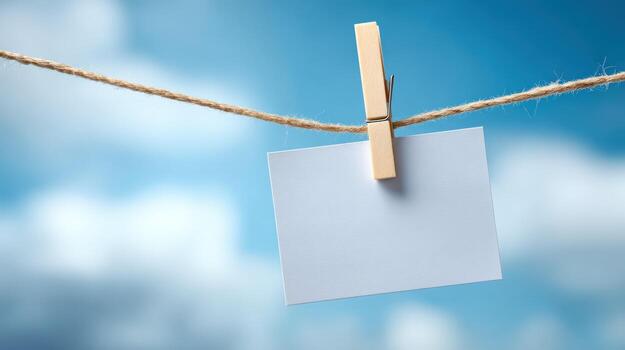 Blank White Card Hanging from Twine with a Clothespin Against a Blue Sky Backdrop photo