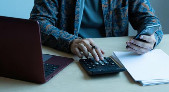 Man Calculating Finances at Desk with Laptop and Phone for Business and Accounting photo