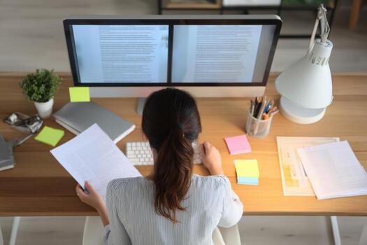 Woman Working at Computer Desk, Reviewing Documents and Analyzing Data for Business Strategy photo