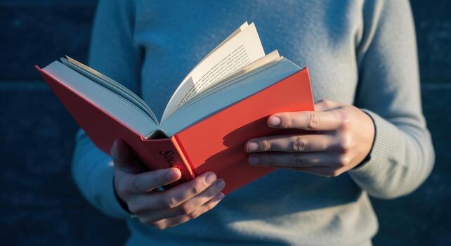 Person Reading a Book with Red Cover Focus on Book, Educational Material, and Casual Learning photo