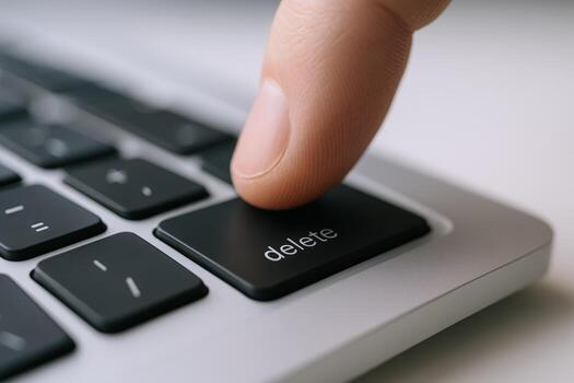 Close-up of a Finger Pressing the Delete Key on a Silver Laptop Keyboard, with Shallow Depth of Field photo