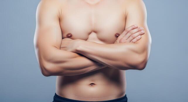 Strong Torso of Athletic Man with Arms Crossed Confidently, Showing Muscle Definition Against a Gray Background photo