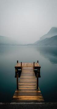 A wooden dock on a lake with foggy mountains in the background photo
