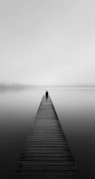 A lone person sits on a dock in the middle of a lake photo