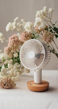 The fan is placed on a wooden stand with flowers in the background photo