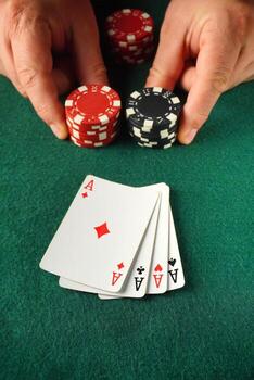 Two hands hold stacks of red and black poker chips while four aces are displayed on a green felt table, indicating a thrilling moment in a card game photo