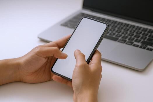 Hands Holding Smartphone with Blank Screen, Laptop Computer Background, Promoting Mobile App, White Background, Technology photo
