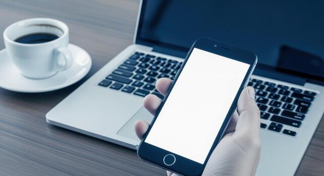 Mobile Phone in Hand with Laptop and Coffee, Showing a Blank Screen for Mockup photo