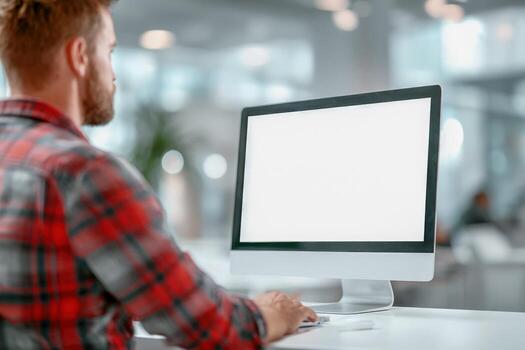 Man working on a computer with blank screen in modern office environment, workspace mockup photo