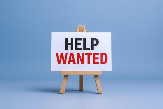 Help Wanted Sign on Easel Against Blue Background Calling for New Employees or Assistance photo