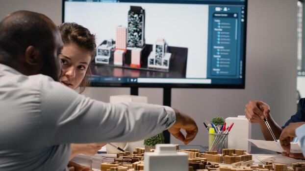 Diverse engineers team go over structural real estate city planning using 3D models to visualize residential layout expansion and infrastructure growth on the table. Innovation hub. photo