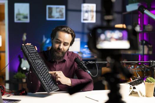 Influencer filming keyboard review in apartment, showing typing capabilities. Technology guru showcasing computer peripheral to audience on niche online channel, looking at functionalities photo