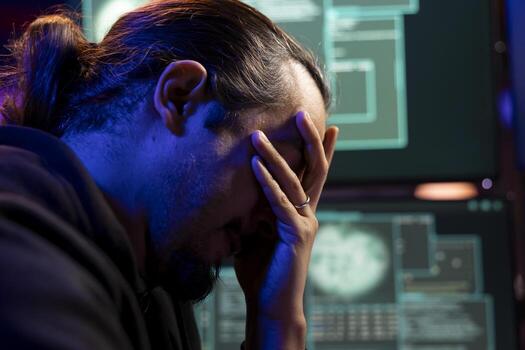 Closeup of sad hacker upset after failing to get malware past antivirus protection. Dejected cybercriminal in underground lair doing face palm, unable to develop data mining script to breach firewalls photo