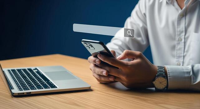 Man using smartphone for online search with a laptop on the table, internet concept photo