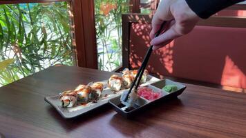 Woman hand takes delicious sushi roll with chopsticks in restaurant closeup. Lady enjoys Asian food for dinner slow motion. Luxury lifestyle video