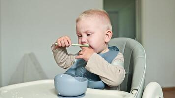 en charmig litet barn åtnjuter en rörig matdags praktiserande självmatning med en färgrik sked, skapande härlig stunder den där bygga varaktig minnen i en familj Hem video