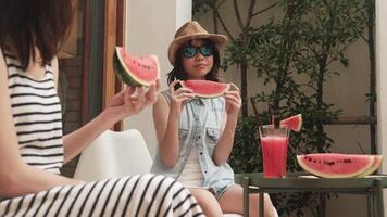 Cheerful Asian family holidays, casual girl and mum in sunglasses enjoy eating fresh watermelons sliced and smoothie drinks, happiness relaxing on vacation, and hot summertime at outdoor terrace. video