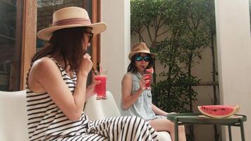 Happy Asian family holidays, casual girl and mum in sunglasses enjoy eating fresh watermelons sliced and smoothie drinks, chilling on vacation, and hot summertime at outdoor terrace. video