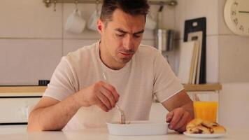 dentro uma acolhedor cozinha, uma homem senta às a mesa e come uma forte servindo do Lasanha. ele focos em dele refeição enquanto bebericando laranja suco, desfrutando uma pacífico hora do almoço momento video
