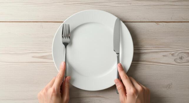 Hands holding cutlery next to an empty white plate on wooden background photo
