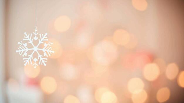 A snowflake hanging from a string in front of a blurred background photo