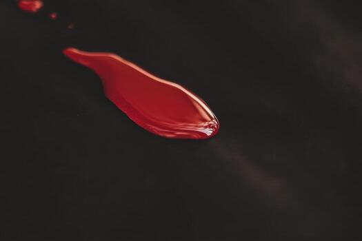 Red paint drips on a black surface during artistic creation process photo