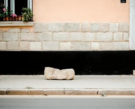 Large rock positioned on a sidewalk near a colorful building with flowers photo