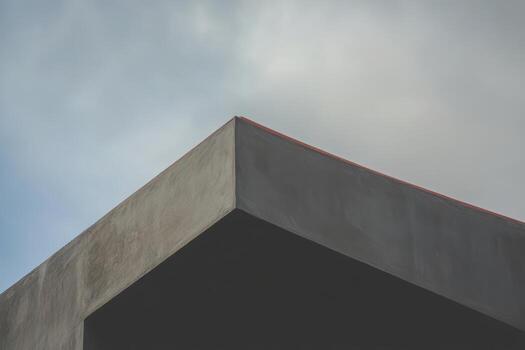A close-up view of a contemporary concrete building's edge meets a cloudy sky photo