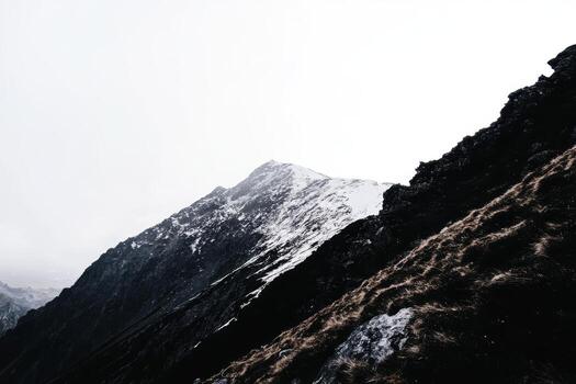 Snow-capped mountain peak rises dramatically under cloudy sky photo