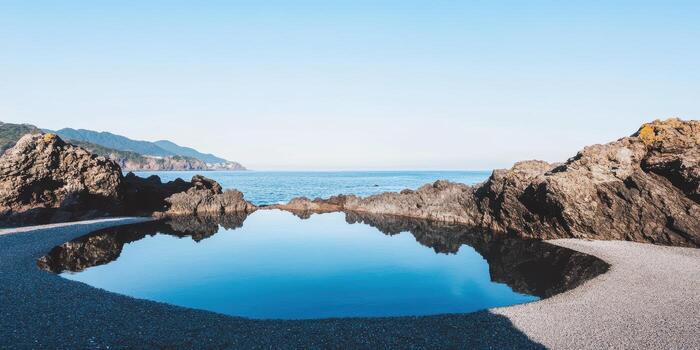 Tranquil tidal pool reflecting blue sky and distant mountains at the coast photo