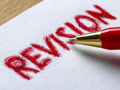 Red ballpoint pen resting on textured paper with the word revision written boldly in red ink to emphasize editing and improvement concepts photo