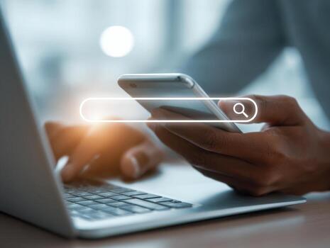 Person using smartphone and laptop with digital search bar overlay representing online browsing and information seeking in modern technology environment photo