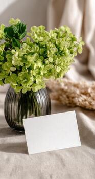 A vase with green flowers and a blank card on a table photo