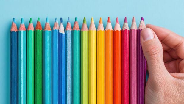 A person holding a rainbow colored pencil in front of a row of colored pencils photo