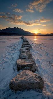 A stone path in the snow with the sun setting behind it photo
