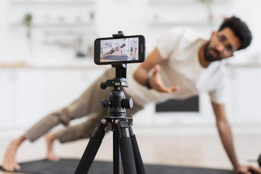 Middle-aged man performs plank exercise while recording fitness tutorial using smartphone camera setup. photo
