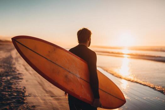 un hombre vestido en un traje de neopreno camina a lo largo el arenoso playa participación un naranja tabla de surf mientras el Dom conjuntos en el fondo, creando un pintoresco noche atmósfera foto