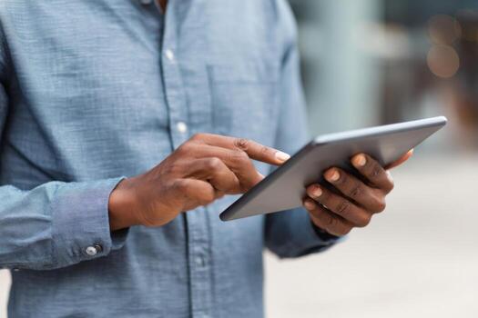 A person stands outside in a contemporary setting, focused on using a tablet with both hands. The surroundings suggest a busy urban atmosphere in daylight photo