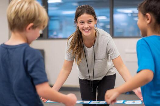 A young teacher is smiling while facilitating a hands-on learning activity with two excited children in a bright classroom space. The kids are focused and participating actively photo