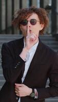shh ser tranquilo por favor. caucásico empresario prensas índice dedo a labios hace silencio Cállate gesto firmar hacer no dice chisme secreto al aire libre. chico con Rizado pelo en céntrico ciudad. negocio gente. video