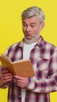 maduro hombre se enfoca atentamente en abierto libro, revelador aturdido curiosidad perplejo mirada. de edad mediana chico en amarillo antecedentes exhibiciones asombrado Guau reacción, reticente a nuevo revelaciones oculto en texto video