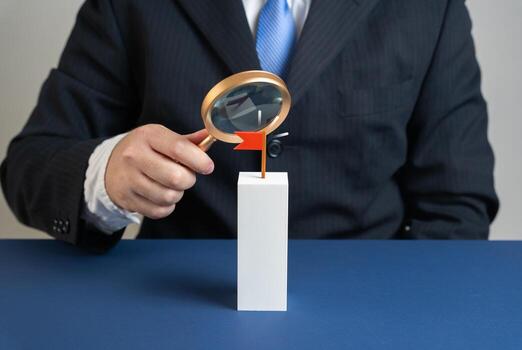 Businessman examines flag target with magnifying glass. Evaluation of target and resources to achieve it. Symbol of planning, performance, data analysis, and strategic decisions. photo