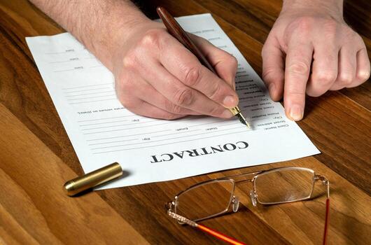Drawing up contract in a working environment on the desktop. Close-up of man hands filling out blank with pen photo