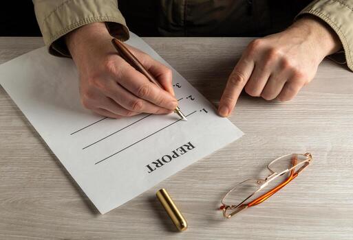 Drawing up report in a working environment on the desktop. Close-up of man hands filling out blank with pen photo