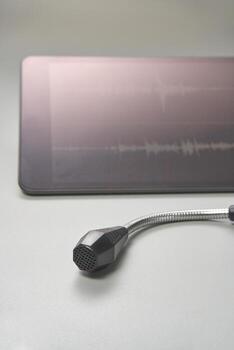 Microphone with tablet displaying sound waveforms on gray surface. photo