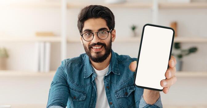 Hello. Happy arab man waving hand and smiling to camera, sitting at workplace at home. Eastern guy gesturing hi and greeting while making call. Modern remote communication concept photo