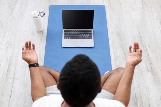Millennial african american guy look at laptop with empty screen on mat on floor with bottle of water and practicing yoga at home. lesson with class, coach remote, training with device, top view photo