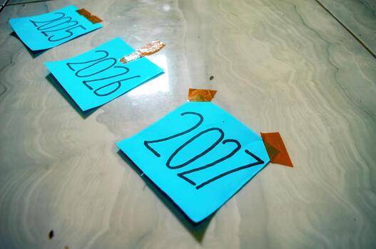 Three blue sticky notes labeled 2015, 2016, and 2017 taped to tiled floor with orange tape symbolizing past years, reflection, and timeline of personal or project milestones photo